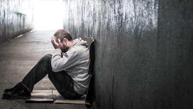 Young homeless male of caucasian ethnicity sitting on the floor of a dark subway tunnel with his hands on his head. Desaturated horizontal colour image with lots of room for copy space. LEV pg 8-9homeless man tunnel 2 iSTOCK