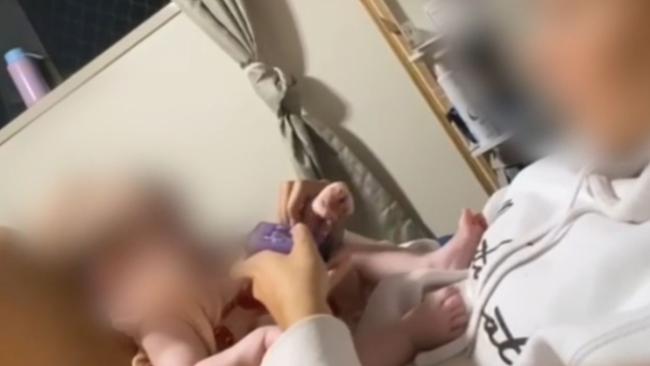 The video shows a girl offering a vape device to a 5-month-old baby, and quickly withdrawing it when the baby moves to put her mouth on the device.