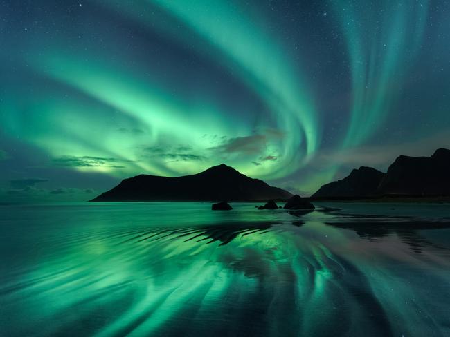 Insight Astronomy Photographer of the Year 2017 shortlist selection: Reflection . Picture:Beate Behnke (Germany) The reflection in the wave ripples of Skagsanden beach mirrors the brilliant green whirls of the Aurora Borealis in the night sky overhead. To obtain the effect of the shiny surface, the photographer had to stand in the wave zone of the incoming flood, and only when the water receded very low did the opportunity to capture the beautiful scene occur. Skagsanden, Lofoten, Norway, 28 October 2016