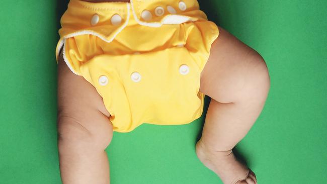 Stock photo of a five month old Baby wearing yellow cloth nappy or diaper (reusable diaper) against green background. Picture: Getty Images