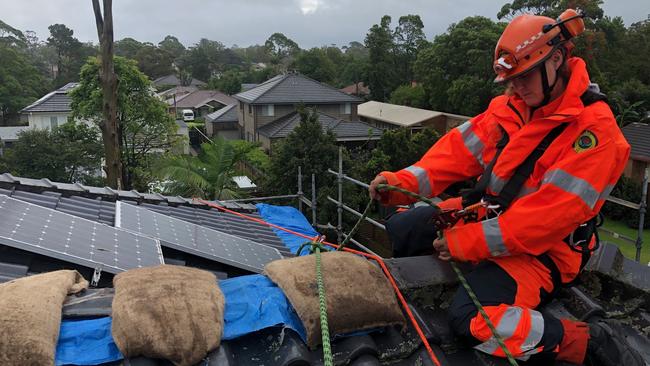 A SES volunteer places sand bags on the tarps to protect the roof from leaking after the storms. Picture: SES