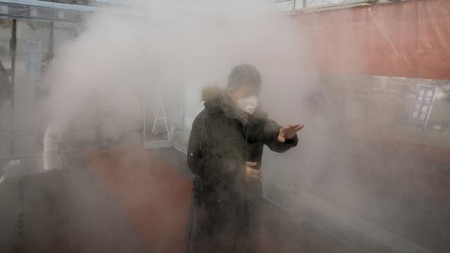 A man walks through a disinfectant spray in order to return home at a residential complex in northern China's Tianjin Municipality on Tuesday. Picture: Chinatopix via AP