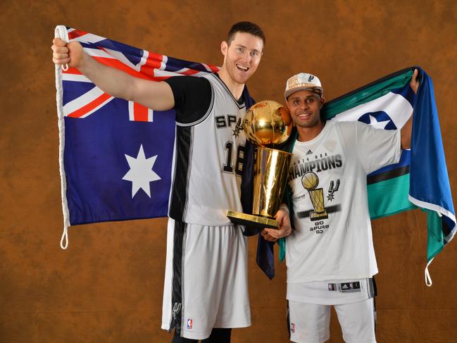 Aron Baynes and Patty Mills of the San Antonio Spurs poses for a portrait with the Larry O'Brien Trophy after defeating the Miami Heat in Game Five of the 2014 NBA Finals.