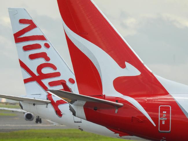 The vertical stabilisers of a Qantas Boeing B737-838 plane, registration VH-VZQ, and a Virgin Australia Boeing B737-8FE plane, registration VH-VUZ, waiting at the northern end of the main runway of Sydney Kingsford-Smith Airport in preparation for departure.  The Qantas plane is heading to Adelaide as flight QF741 and the Virgin plane is heading to Adelaide as flight VA428.  In the background is another Virgin B737-8FE plane. This image was taken from Nigel Love Bridge, Mascot on a sunny afternoon on 3 December 2023.