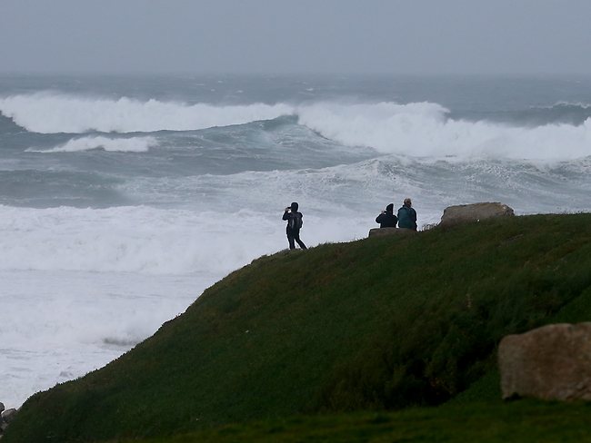 People stop to look at the stormy seas off Fistral Beach in Newquay, Cornwall.