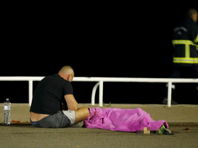 A man sits next to a body seen on the ground. Picture: Eric Gaillard/Reuters