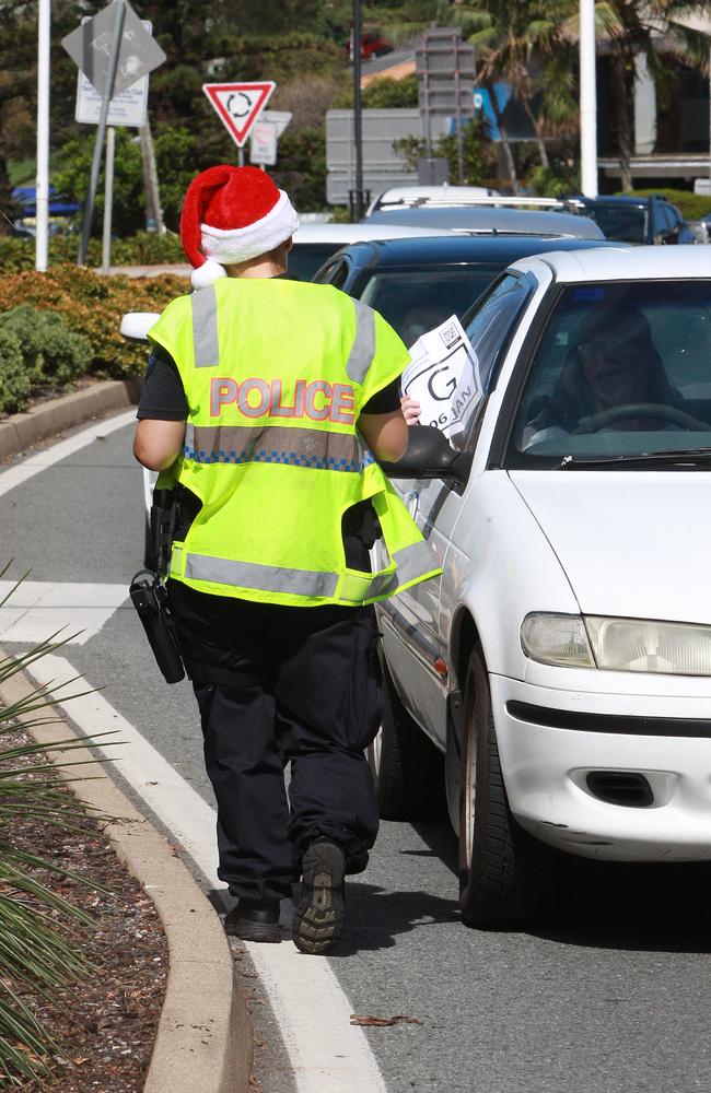 A Queensland police officer wearing a Santa hat inspects the paperwork of people attempting to cross the Queensland border from NSW. Picture: Mike Batterham