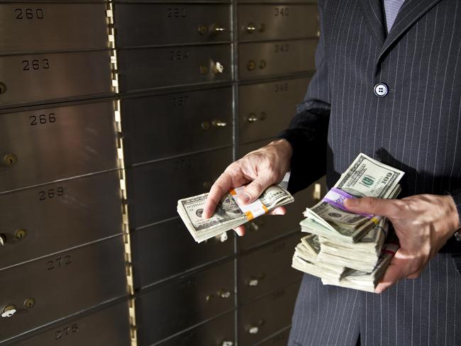 Man holding big stack of US paper currency by safety deposit boxes.