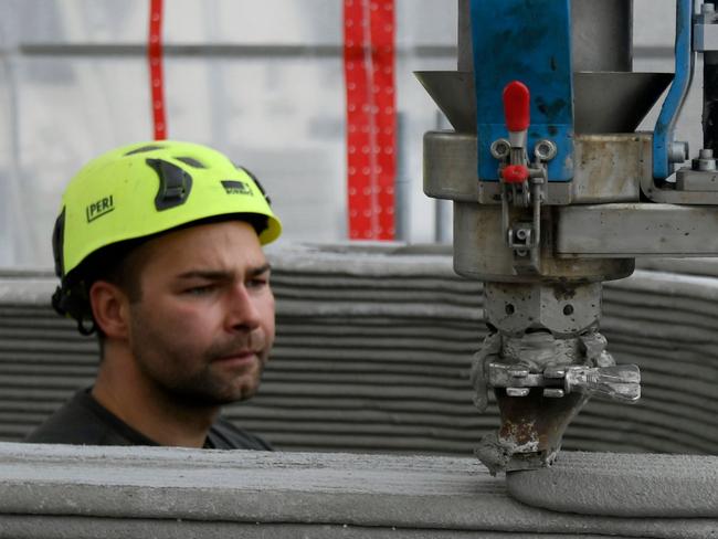 A man watches the head of the 3D printer which applies the next layer of concrete to the walls of a house at the construction site in Beckum, western Germany, on November 26, 2020. - According to North Rhine-Westphalia's state government, Germany's first residential building constructed by 3D printing or additive manufacturing technique is currently being built in Beckum. (Photo by Ina FASSBENDER / AFP)