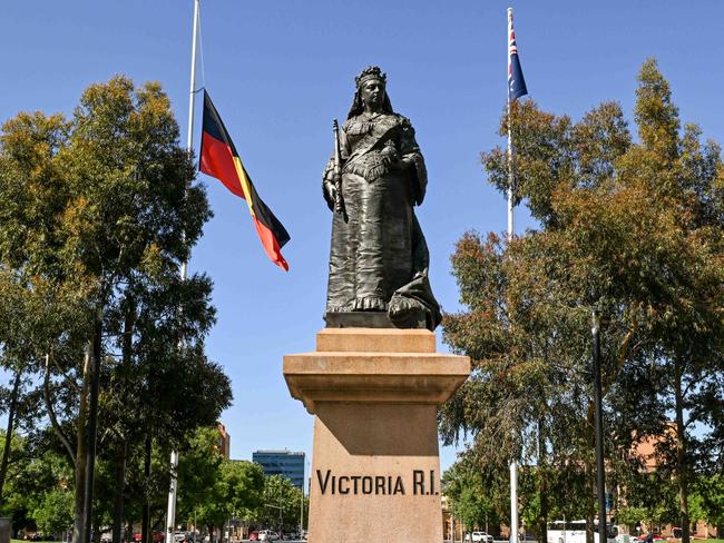 ADELAIDE, AUSTRALIA - NewsWire Photos October 18, 2023: A statue of Queen Victoria in front of the Aboriginal flag at half mast and the Australian flag at full staff in Victoria Square. The Adelaide city council has decided to fly the Aboriginal flag at half-mast on the Town Hall and in Victoria Square after SaturdayÃs referendum defeat. Picture: NCA NewsWire / Brenton Edwards