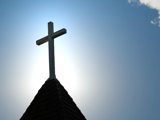 A wood cross on an old church steeple backlighted by a rising sun. Some copy space.