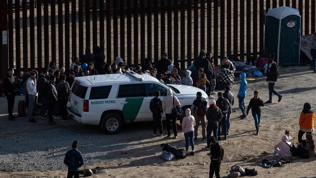 Migrants gather around a US border patrol vehicle between border fences waiting to be processed by US authorities, as seen from Tijuana, Baja California State, Mexico, on May 6, 2023.