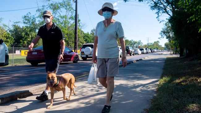 A drive-thru testing clinic has been commissioned at Marrara to deal with the uptick in required testing during the Darwin lockdown. A couple walk their dog past the snaking line of people waiting to be tested. Picture: Che Chorley