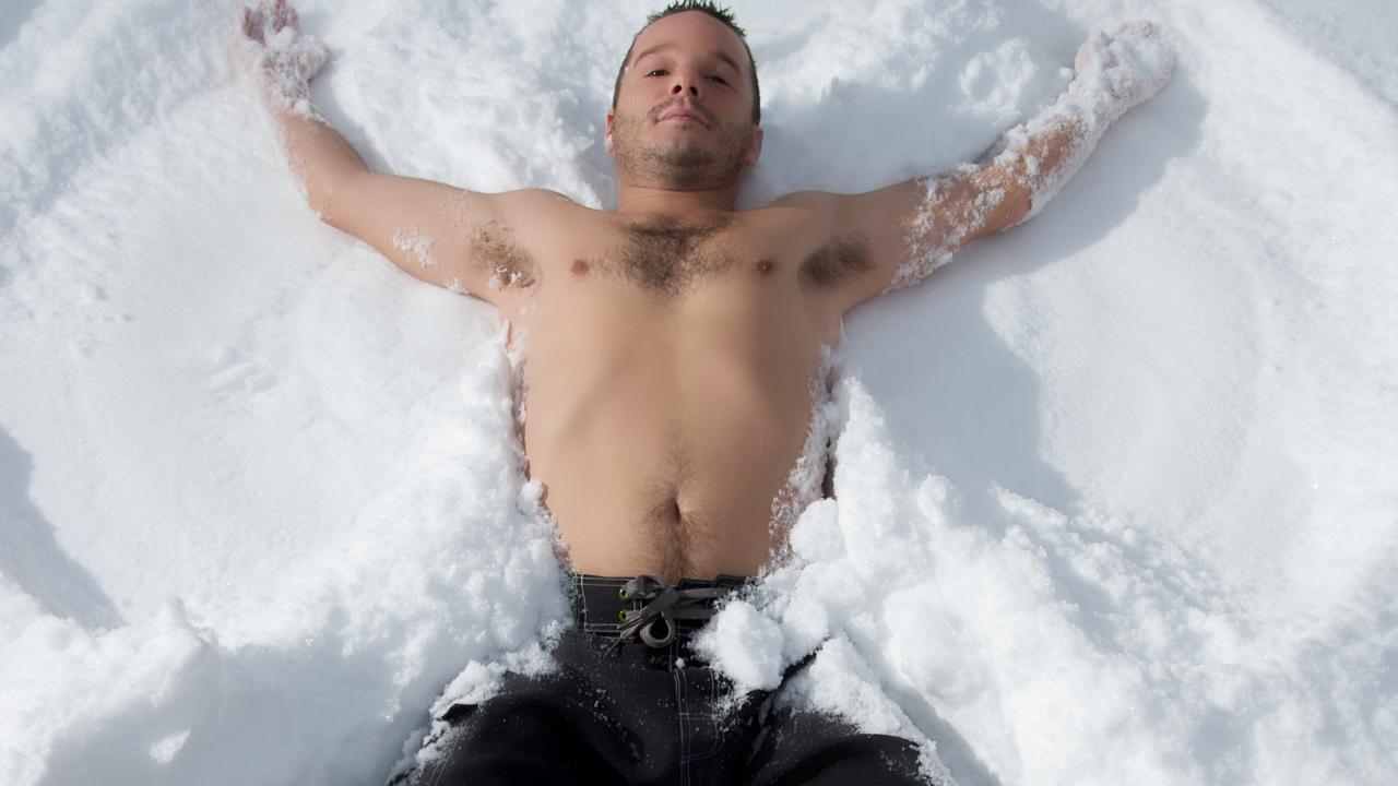 A man makes a snow angel while just wearing shorts.