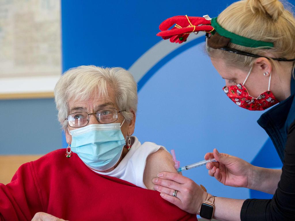 A nurse (R), in her festive mask and antlers, inoculates an 86 year old (L) mail room worker with the Moderna vaccine. Picture: AFP