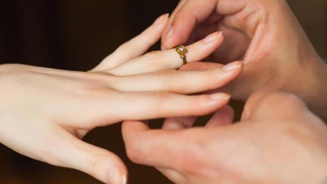 Close up on man putting on ring on his fiances finger during marriage proposal