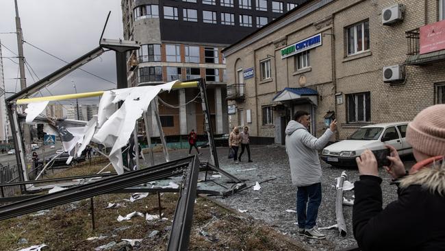 People take photos of damage caused by a Russian rocket attack on Kyiv.