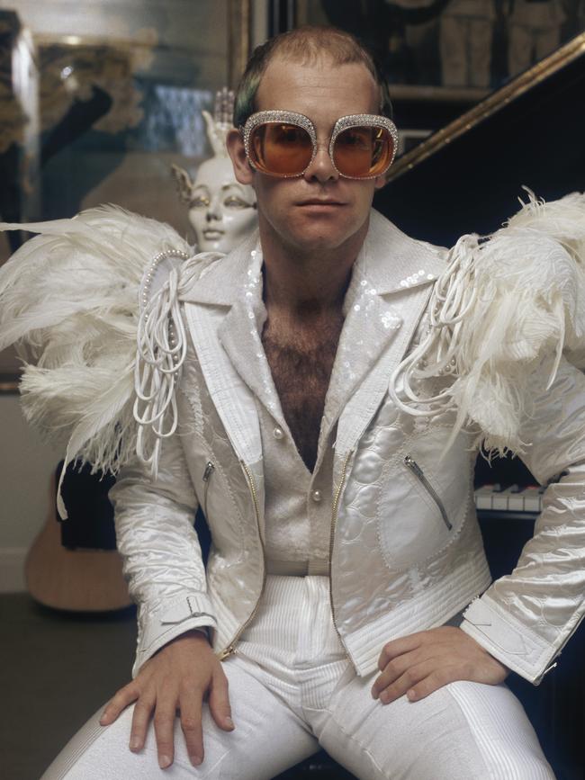 Elton in a white suit with feather trim and rhinestone encrusted glasses in 1973. Picture: Getty Images