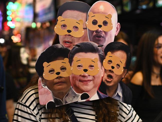 A woman wearing several masks mocking Hong Kong Chief Executive Carrie Lam (bottom L) and China's President Xi Jinping (bottom C). Picture: AFP