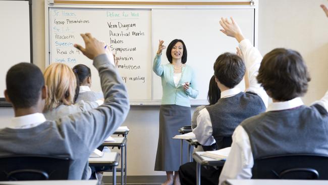 School children (14-18) raising hands in class