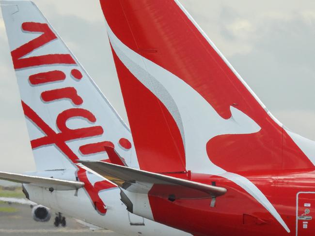 The vertical stabilisers of a Qantas Boeing B737-838 plane, registration VH-VZQ, and a Virgin Australia Boeing B737-8FE plane, registration VH-VUZ, waiting at the northern end of the main runway of Sydney Kingsford-Smith Airport in preparation for departure.  The Qantas plane is heading to Adelaide as flight QF741 and the Virgin plane is heading to Adelaide as flight VA428.  In the background is another Virgin B737-8FE plane. This image was taken from Nigel Love Bridge, Mascot on a sunny afternoon on 3 December 2023.