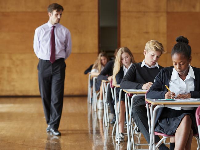 Teenage Students Sitting Examination With Teacher Invigilating