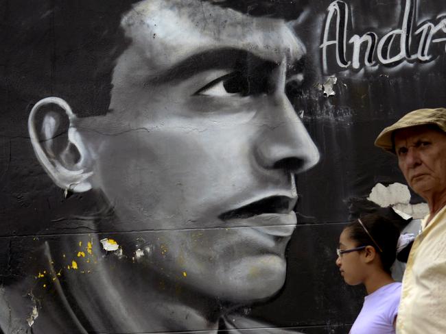 People walk by a mural painting depicting the late Colombian footballer Andres Escobar at the street in Medellin, Antioquia department, Colombia on July 1, 2014. Escobar was shot dead twenty years ago, upon the team's return from the FIFA World Cup in the United States where he had scored an own goal during the Colombia vs United States match. AFP PHOTO/Raul ARBOLEDA