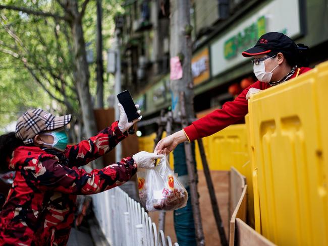 A vendor hands food to a customer over a barricade separating a residential compound in Wuhan yesterday. Picture: AFP