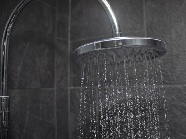 Modern large shower head spraying water, black slate tiled wall behind.Large shower head spraying water - Stock image ipad generic