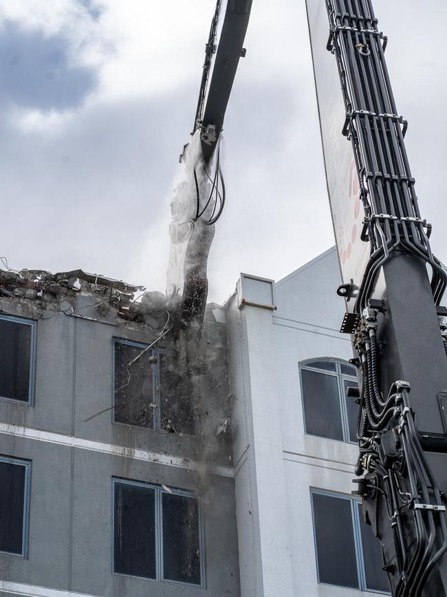 The excavator rips through the facade of the building, collapsing it floor-by-floor.