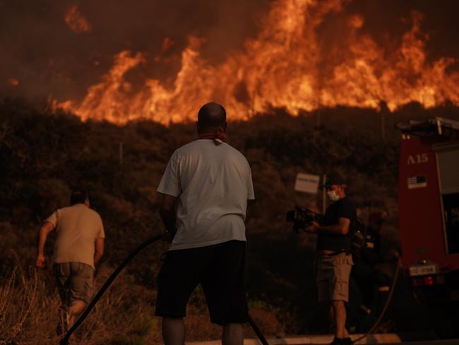 Firefighters and volunteers work to extinguish a burning field during a wildfire in Saronida, south of Athens, Greece, on Monday, July 17, 2023. A fire near Athens is threatening homes, as strong winds and high temperatures fuel the blaze. Photographer: Nick Paleologos/Bloomberg via Getty Images