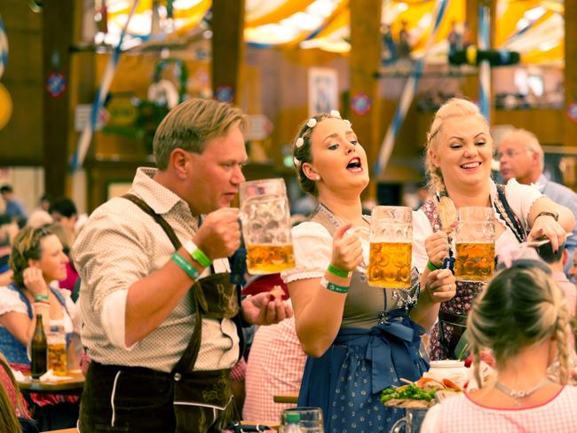 EMBARGO FOR TWAM 17 SEPTEMBER 2022. FEE MAY APPLY.  Munich, Germany - September 29, 2016: Oktoberfest in Munich, Germany. A group of young people in beer hall, celebrating Oktoberfest on Theresienwiese. People are dressed in traditional clothes and holding beer glass. The Oktoberfest is the largest fair in the world and is held annually in Munich.