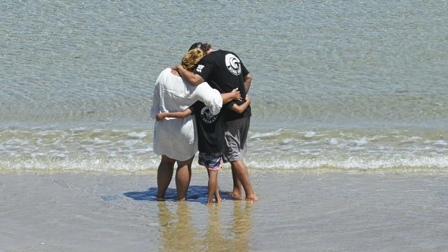 The parents and younger brother of Khai Cowley hug after returning sand collected from surf beaches around South Australia back to the sea during his memorial at Seaford. Picture: NCA NewsWire / Mark Brake