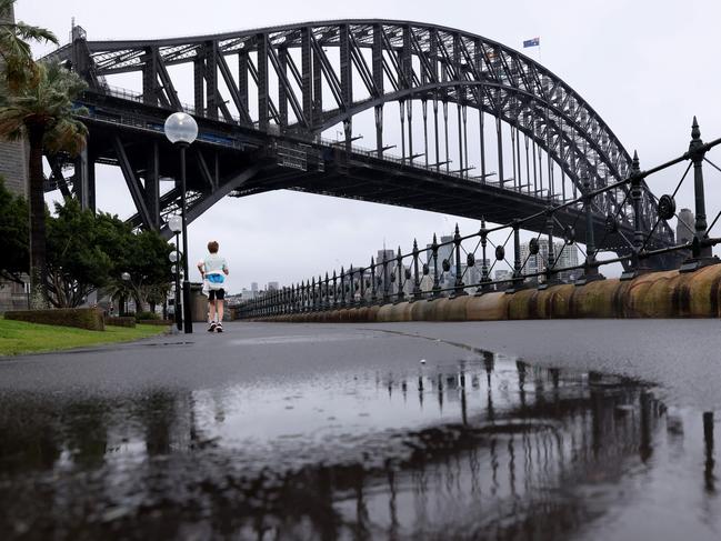 SYDNEY, AUSTRALIA - NewsWire Photos OCTOBER 6, 2022: A person walks in the rain with the Sydney Harbour bridge pictured in the background.Picture: NCA NewsWire / Damian Shaw