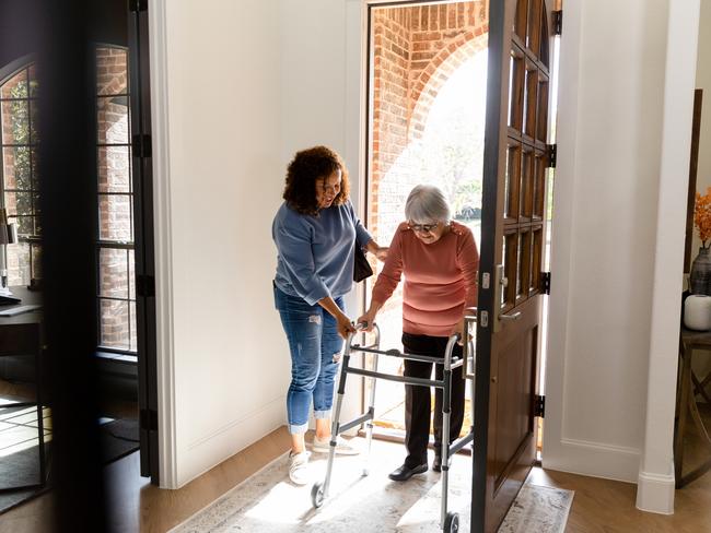 The mid adult woman helps her senior adult friend carefully enter her home.