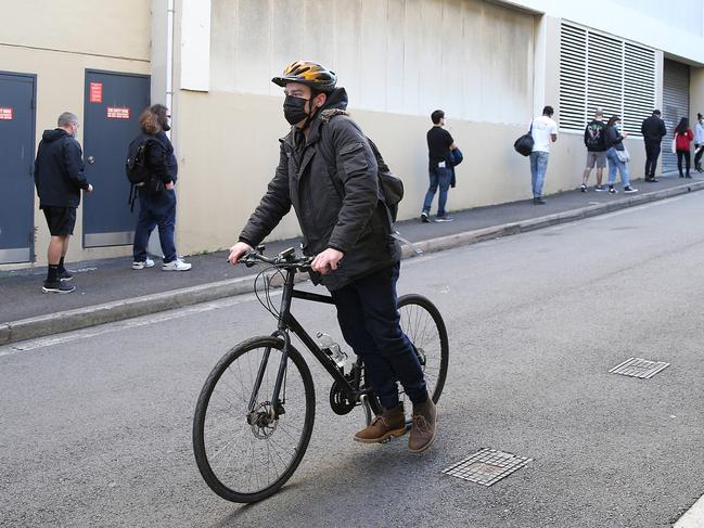 SYDNEY, AUSTRALIA - NewsWire photos AUGUST 07, 2021: A man coasts his bike past people waiting in a 1.5 hour single file line at the Glebe Vaccination hub in Sydney. NSW has recorded 319 new COVID-19 cases and an additional five deaths. Picture: NCA NewsWire / Dylan Coker