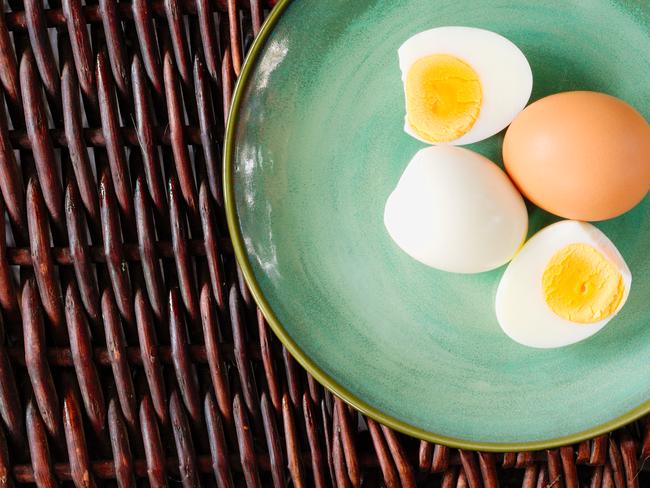 Hard-boiled egg cut and piled on egg slicer and full egg with shell on green plate or dish.