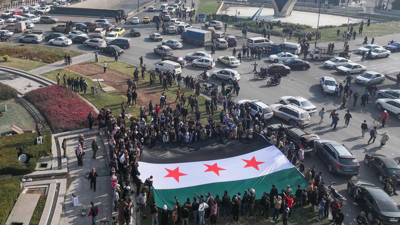 People celebrate holding a large Syrian opposition flag at Umayyad Square in Damascus on December 9, 2024. Syrians flocked to the main square of the capital city Damascus on December 9 to mark what many regard as a long-awaited new dawn after the fall of president Bashar al-Assad. Assad fled to Russia the day before after a lightning offensive spearheaded by Islamist rebels ousted him from power, opening a new chapter in Syria's history after five decades of rule by his clan. Picture: OMAR HAJ KADOUR / AFP)