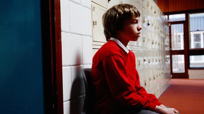 A boy sits out in the corridor after behaving badly in the classroom.