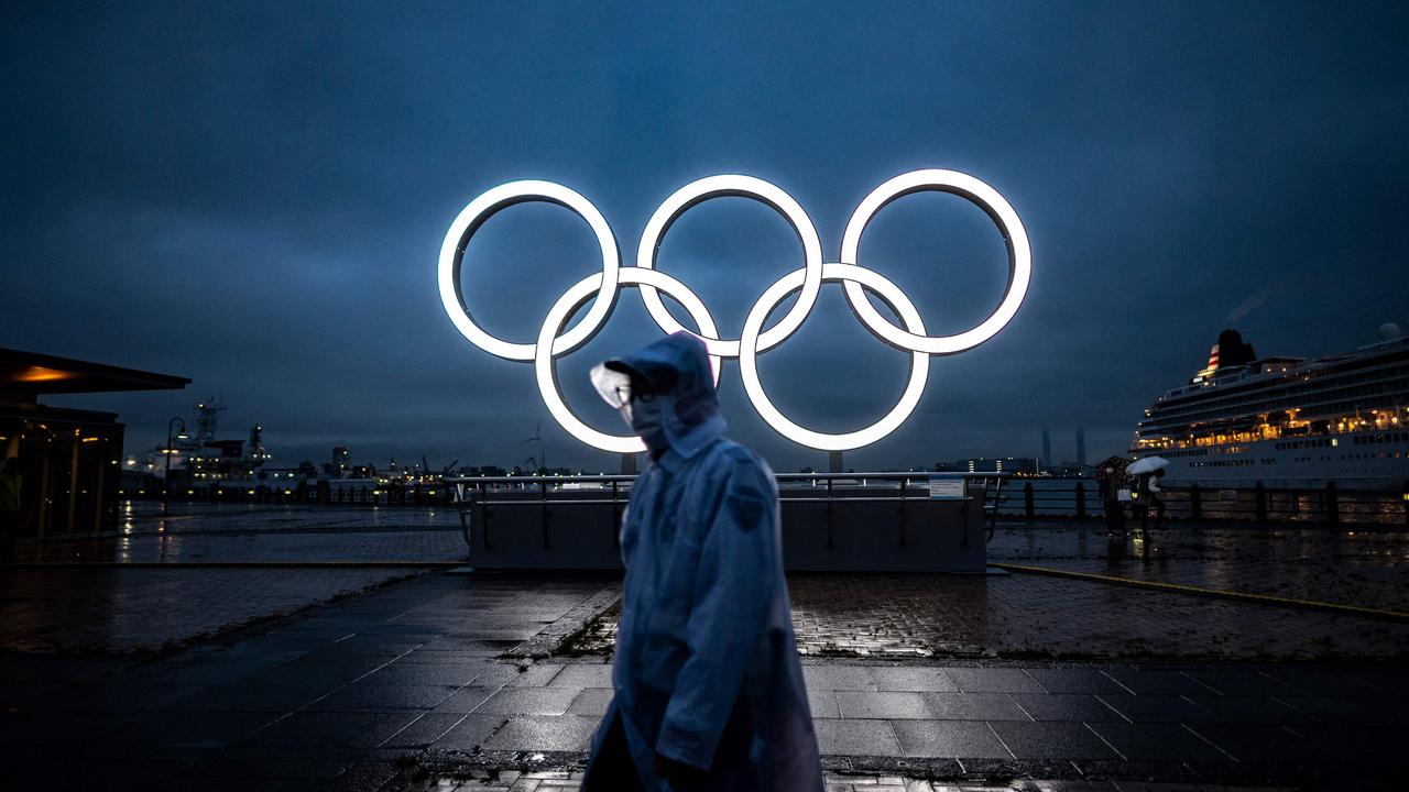 A man walks past the Olympic Rings lit up at dusk in Yokohama on July 2, 2021. (Photo by Philip FONG / AFP)