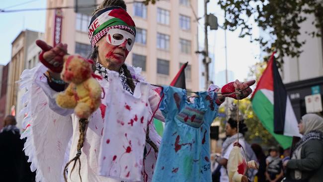 A protester holds up clothing with red marks to signify the deaths of children. Picture: NCA NewsWire / Valeriu Campan