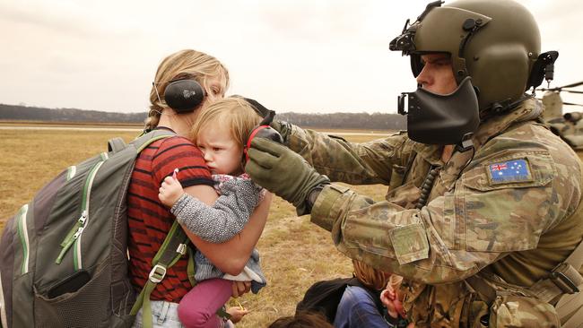 An army Chinook crew member puts ear protection on a child before boarding the helicopter to Sale. Picture: David Caird