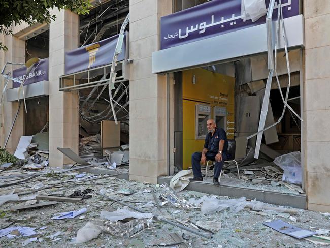 A man sits at the entrance of a damaged bank. Picture: Anwar Amro/AFP