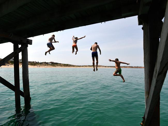 Swimmers jump from the Port Noarlunga jetty as the day warms up. Picture: AAP / David Mariuz