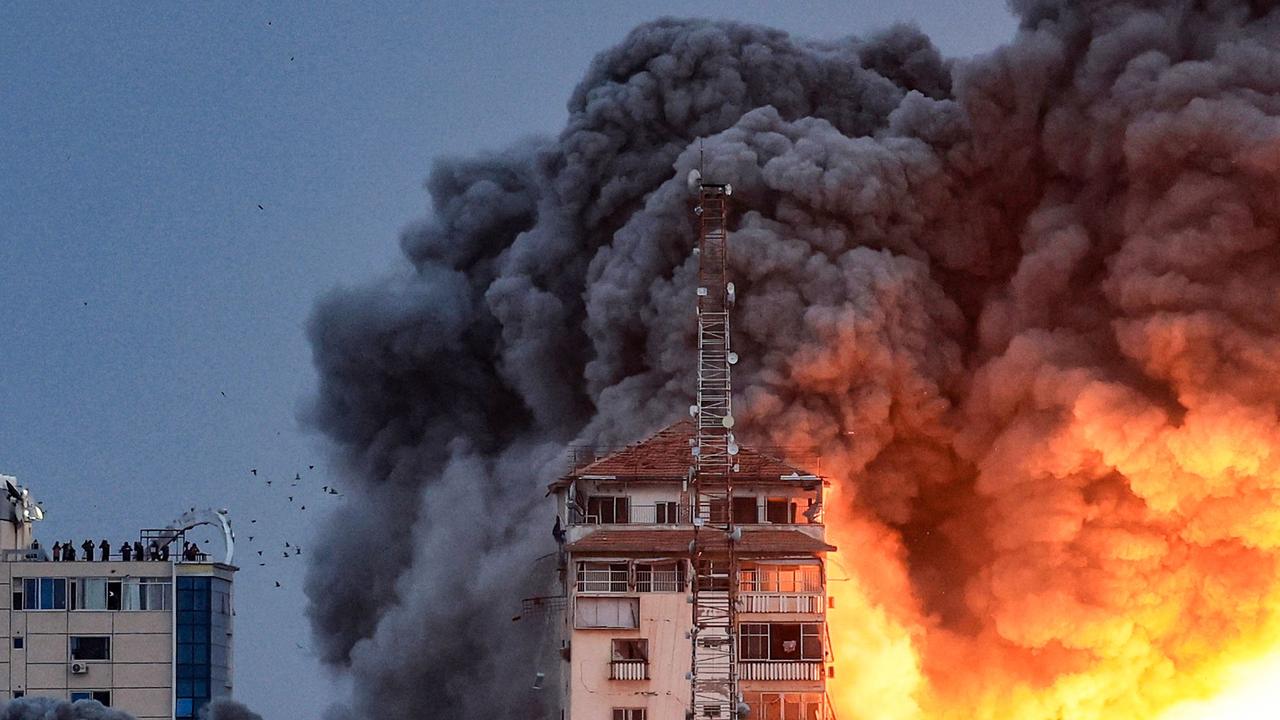 People standing on a rooftop watch as a ball of fire and smoke rises above a building in Gaza City on October 7, 2023 during an Israeli air strike. Picture: AFP