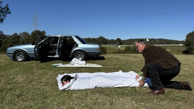 Bronwyn podcast investigative reporter Hedley Thomas, with a 1987 Ford Falcon XF similar to the one owned by Jon Winfield, wraps The Australian’s Video Editor Bianca Farmakis in a sheet for a recreation of Judy Singh’s extraordinary eyewitness account.