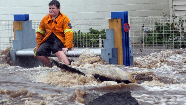 A boy sits on a bench on the main street at Railton and watches the flood waters surge along in 2011.