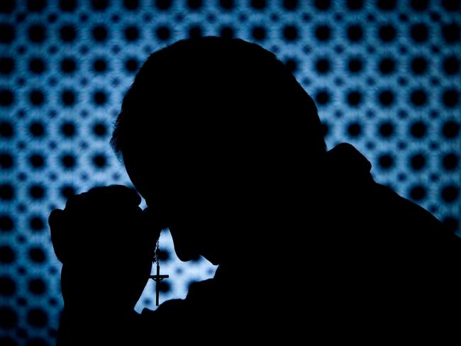 Priest in confession booth with cross in hand. Desaturate the blue for a nice black and white image. The mesh screen is between the camera and priest.