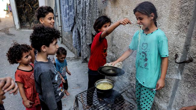 A girl feeds another a spoonful of instant noodles from a pot cooking on a fire in a make-shift oven from a recycled barrel, in Rafah in the southern Gaza Strip on October 31.