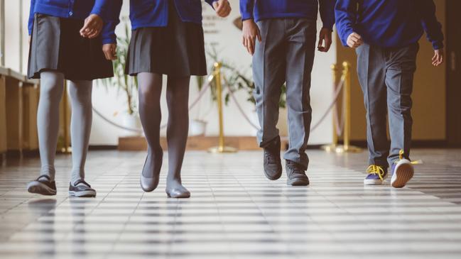 Cropped image of school kids in uniform walking together in a row through corridor. Focus on legs of students walking through school hallway.